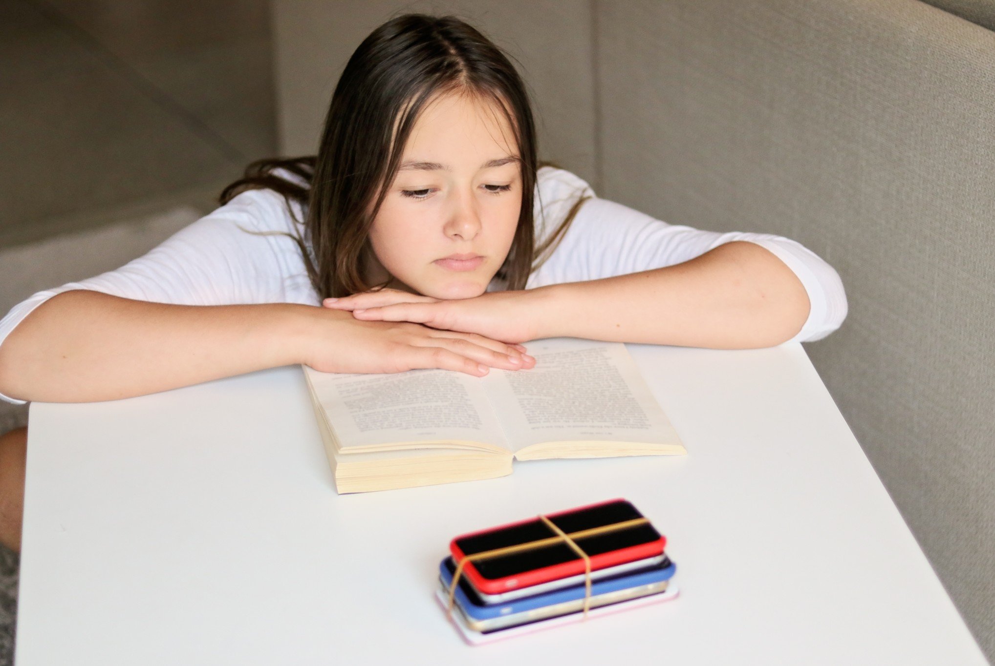 social-media-and-gadget-detox-sad-preteen-girl-reading-book-and-looking-at-pile-of-smartphones-at_t20_Oz4JPp.jpg
